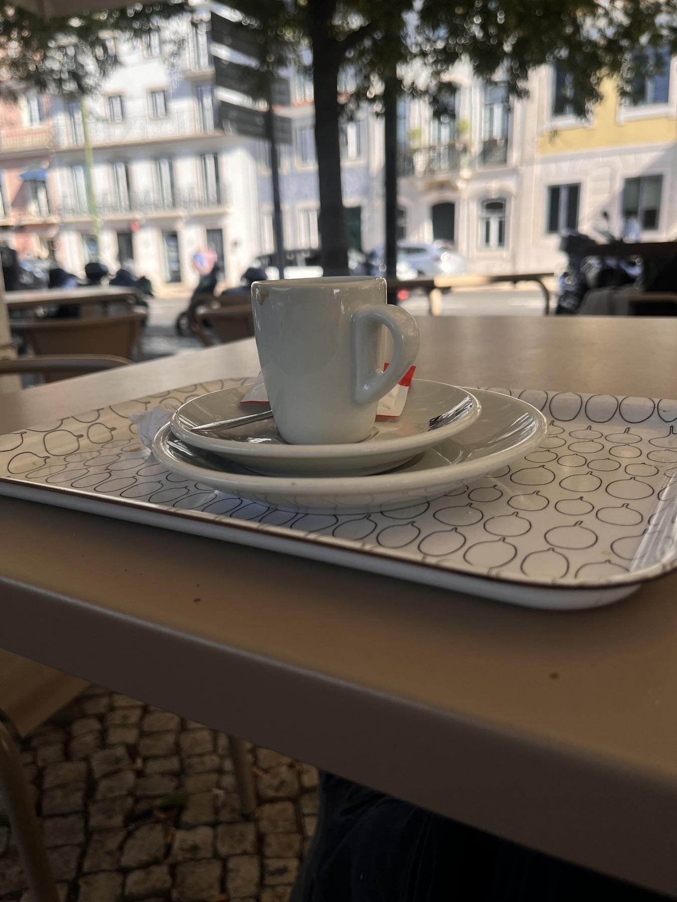 Espresso cup and empty plate sitting on a tray on a table outside, a busy street behind