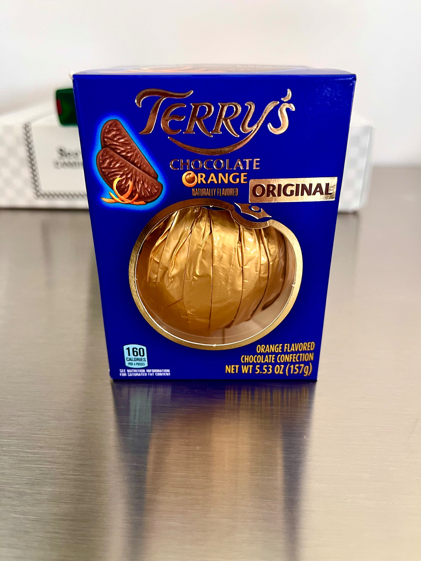 A boxed, blue box,Terry’s Chocolate Orange confection on a reflective metallic surface.