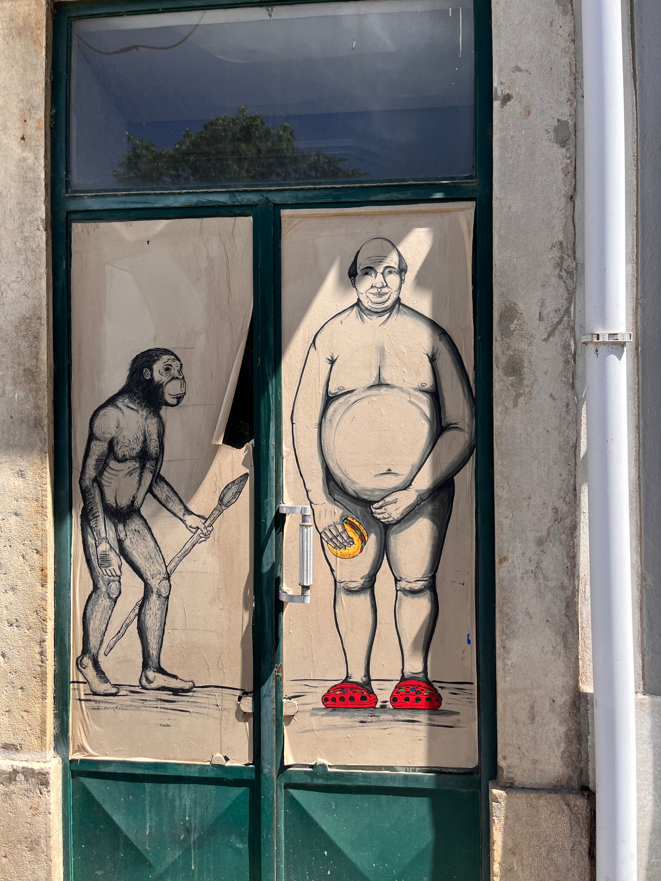 Graffiti art on a door depicting an evolutionary transition from an ape holding a spear to a modern human wearing a beanie and Crocs, while holding a fast-food sandwich and with his hand over his genitals