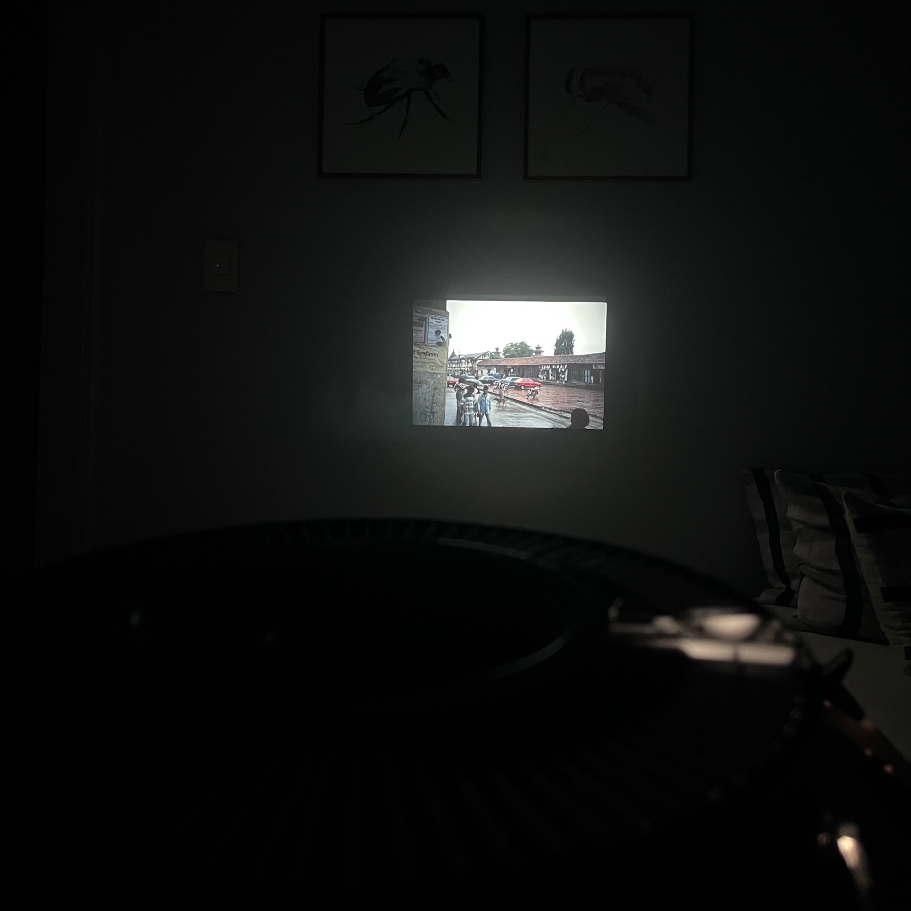 A dark room with a slide being projected onto a wall. In the foreground are lights from the projector, from where the photo is being taken