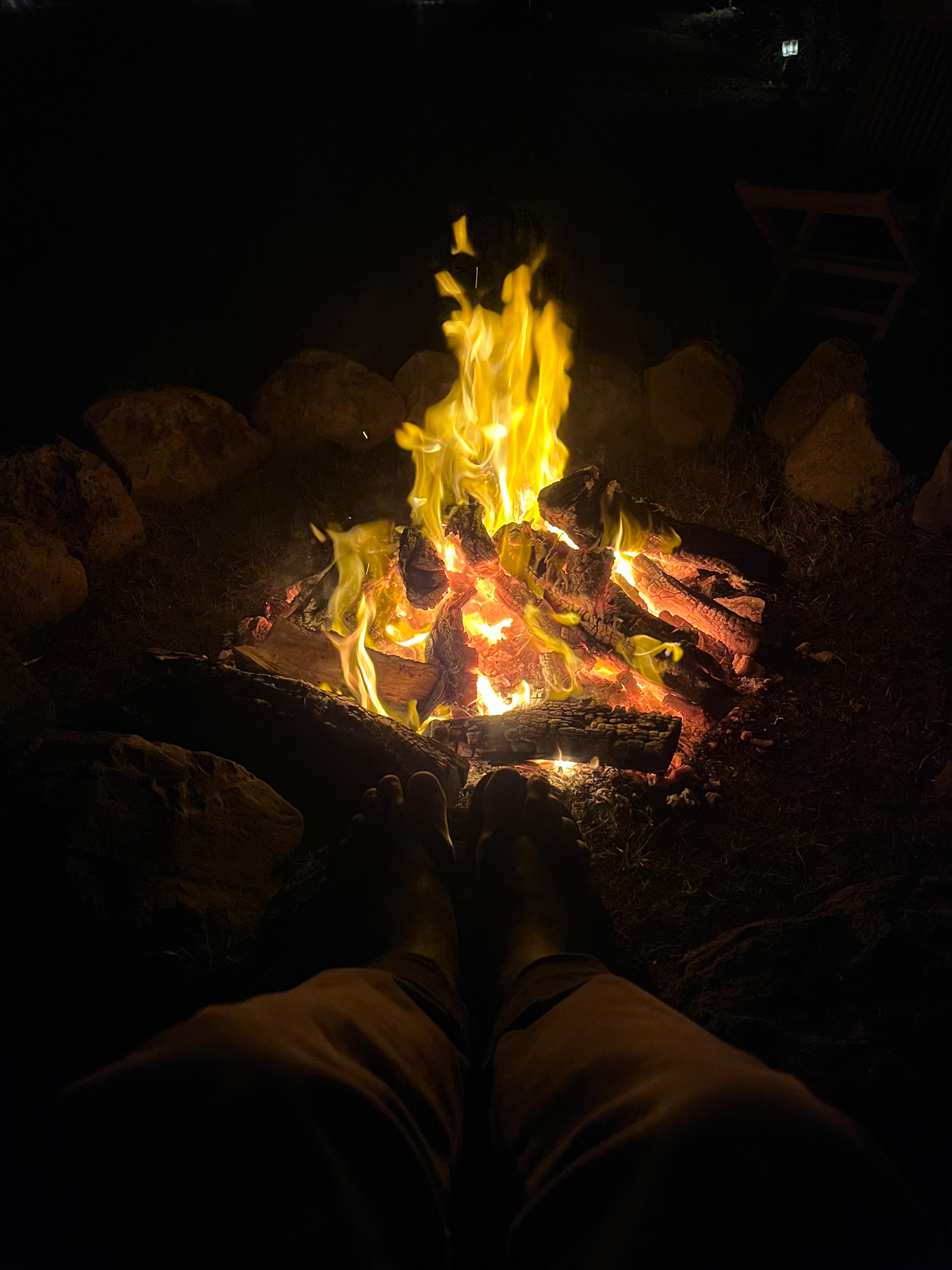 Resting and warming my feet on rocks around a campfire, at night.