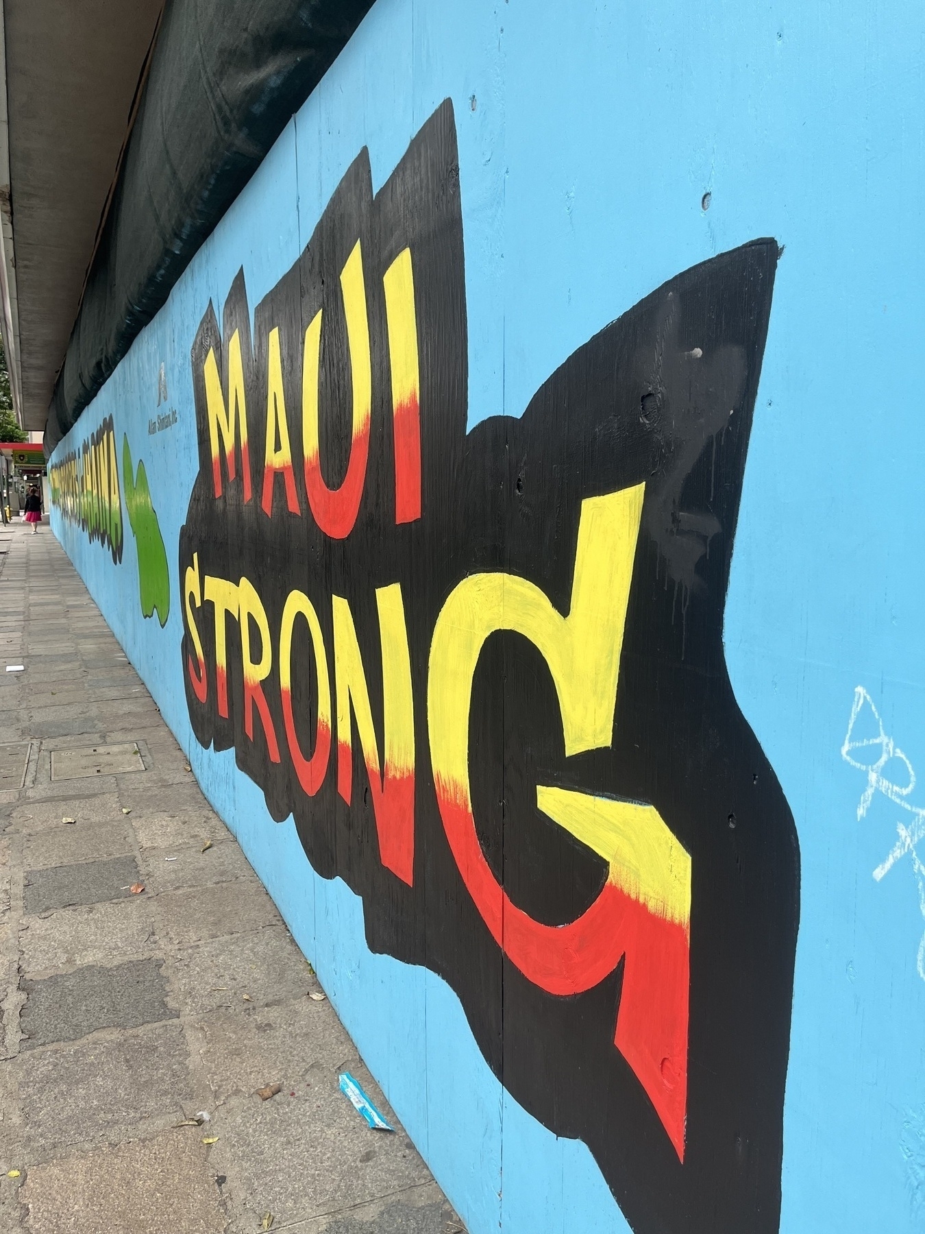 A big board across the front of a building, painted blue with the words Maui Strong painted in big letter along with a map of Maui
