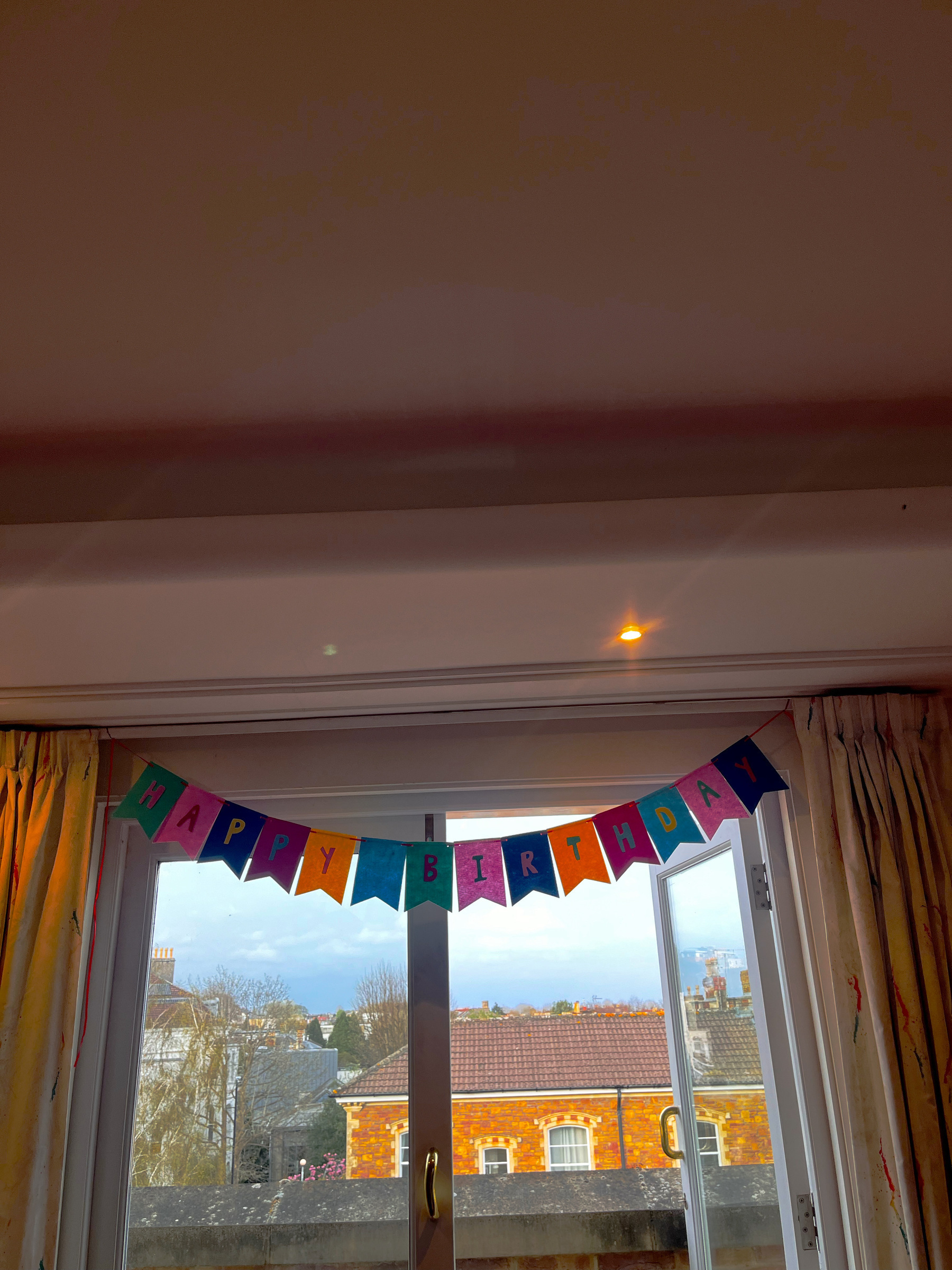 A series of small flags on a piece of string spelling out Happy Birthday. Strung above an open glass door with a view to outside