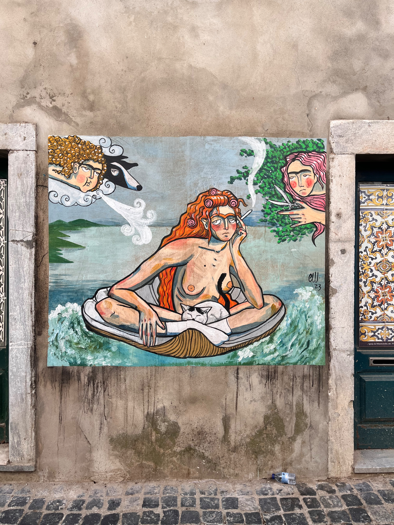 Street art mural depicting a topless woman with red hair and eyeglasses lounging on a lifebuoy in water, accompanied by a white cat, with stylized faces of two people in the clouds above. The artwork is framed by a real door