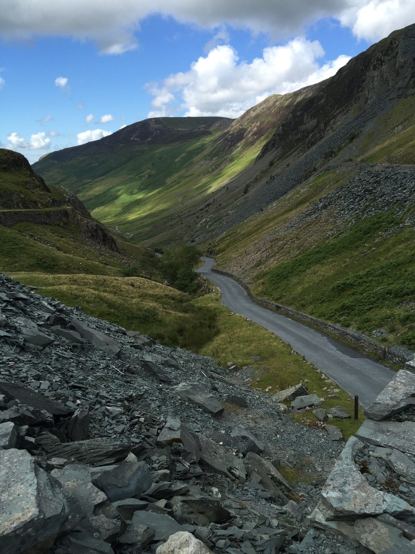 A road running through the mountains of the Lake District with slate in the foreground.