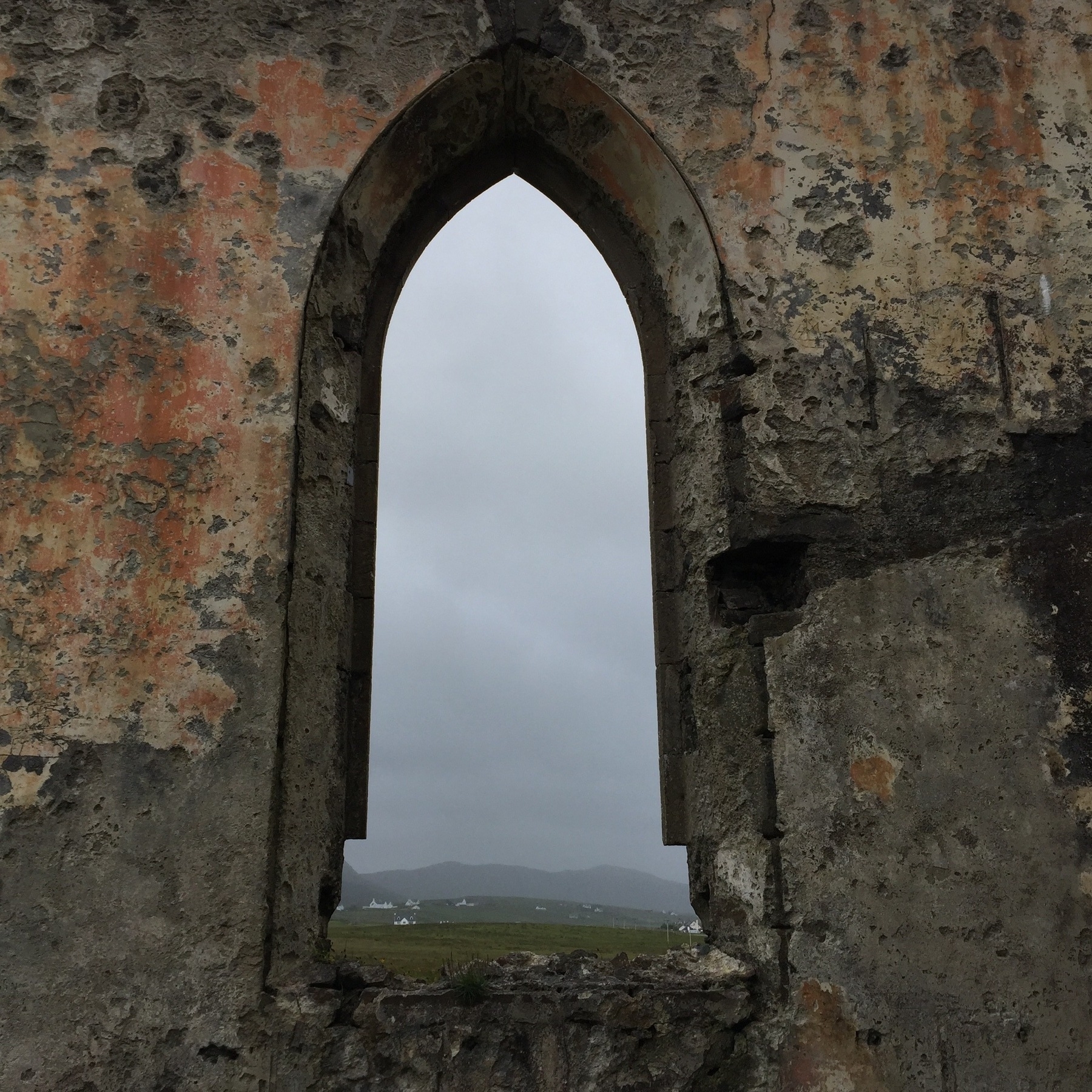 A frame of an old church window in the ruins of a church, looking out on an overcast, wet and windy day