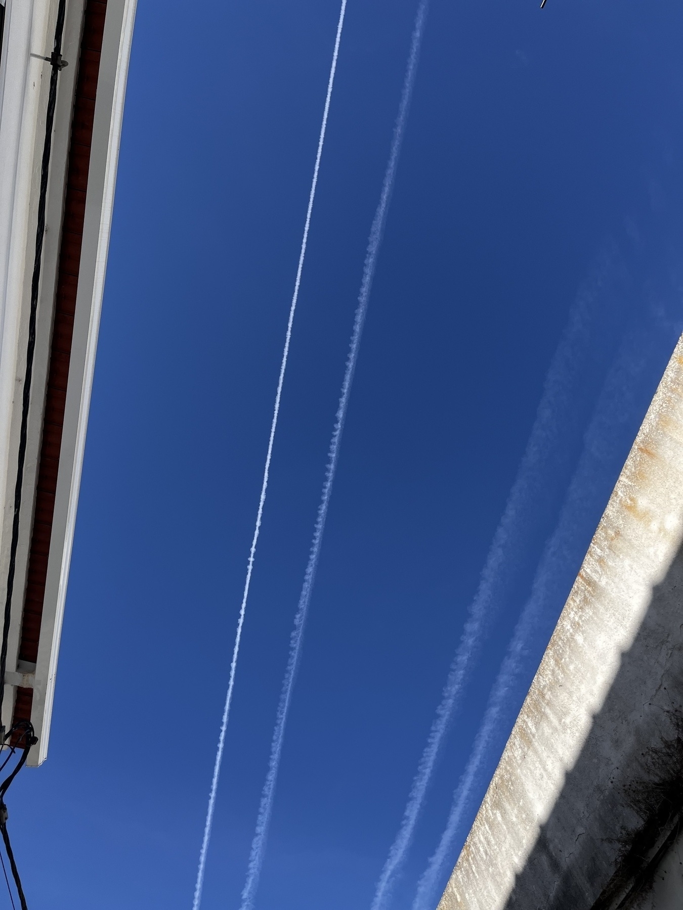 Parallel Contrails against blue sky with the edge of roof tops on both sides of the image