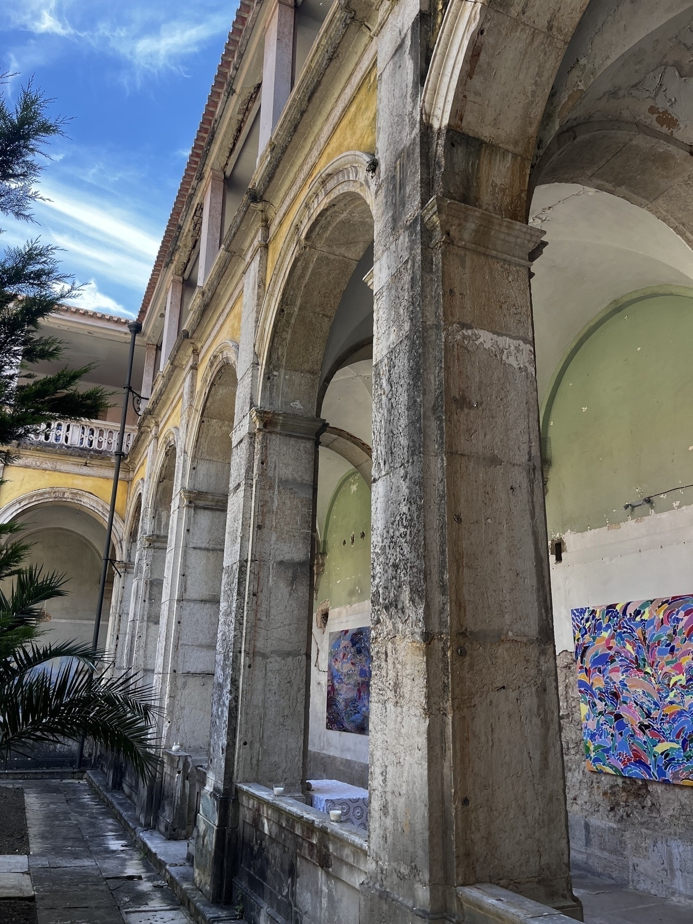 A cloister in the Estrela Basilica showing arches, part of the garden and some paintings from an exhibition